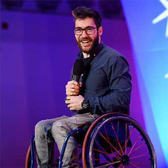 person in wheelchair holding a mike and looking at camera
