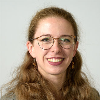 person with long hair and glasses smiling at the camera