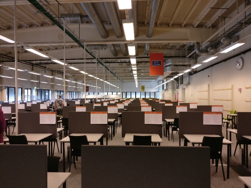 Photograph of NTNU Eksamen (Exam) building interior with long rows of desks and chairs set up for exams 