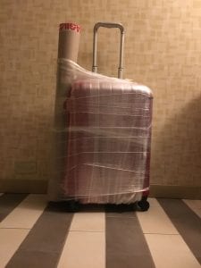 Photograph of suitcase and poster tube shrinkwrapped in a motel room