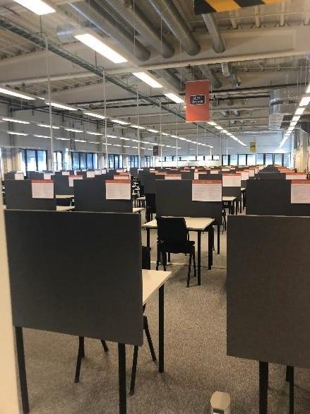 Colour photograph of the interior of the Exam Factory showing rows of screened desks with chairs with notes on the desk screens